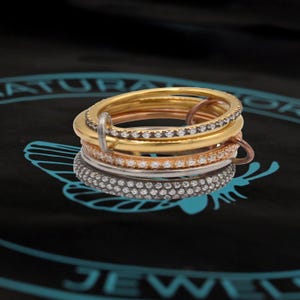 Pode incluir: Quatro anéis empilháveis com uma banda incrustada de diamantes. Os anéis são de ouro, ouro rosa e prata.