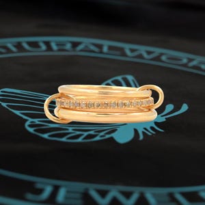 Könnte beinhalten: Drei goldene Ringe mit einer Reihe kleiner Diamanten am mittleren Ring.