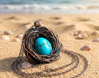 May include: A pendant necklace featuring a bright turquoise oval stone with dark veining, encased in a nest-like structure made of coiled dark copper-toned wire. The pendant hangs from a matching dark metal chain link necklace.