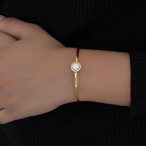 May include: A gold bangle bracelet with a single round clear stone surrounded by smaller stones.