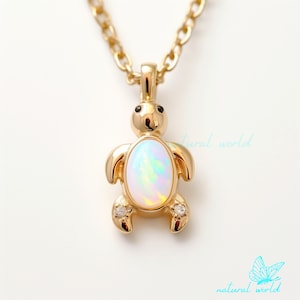 Puede incluir: Un collar de oro con un pequeño colgante de tortuga con una piedra de ópalo blanco y dos pequeños diamantes. La tortuga está mirando hacia adelante con la cabeza levantada.