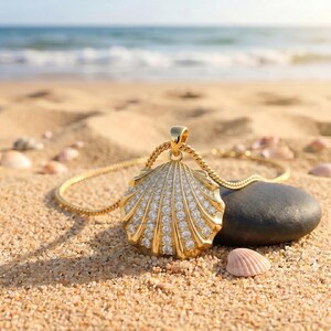 May include: A gold-toned pendant shaped like a scallop shell, featuring rows of embedded clear stones. The pendant is attached to a matching gold-toned rope chain necklace. The design mimics the natural ridges of a seashell with a metallic finish.