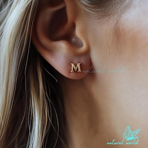 May include: Gold initial letter 'M' stud earrings. The earrings are small and delicate, perfect for everyday wear.