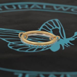 Op de afbeelding: Een gouden ring met een band van turquoise stenen. De ring is dubbel gevat, met een dunnere zilveren band onder de gouden band.