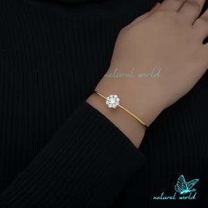 May include: A gold bangle bracelet with a clear crystal flower design. The bracelet is open and has a simple, elegant design.