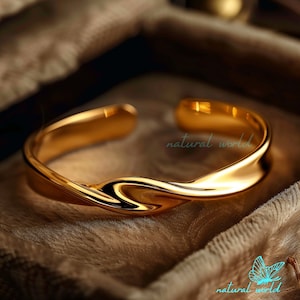 Puede incluir: Un brazalete de oro retorcido. El brazalete está hecho de un metal liso y brillante y tiene un diseño simple y elegante.