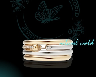 Könnte beinhalten: Ein Gold- und Silberring mit drei Bändern und zwei kleinen Diamanten. Der Ring ist vor einem schwarzen Hintergrund mit einem Schmetterling und dem Text "Jewel World" und "natural world" platziert.