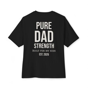 Op de afbeelding: Zwart T-shirt met witte tekst: "PURE DAD STRENGTH BUILT FOR MY KIDS EST. 2026". De t-shirt met korte mouwen heeft een ronde hals. De tekst is gecentreerd op de achterkant van het kledingstuk.
