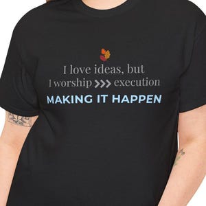May include: Black t-shirt with the text "I love ideas, but I worship >>> execution MAKING IT HAPPEN" in grey and blue text. There is a small graphic of three autumn leaves in the top center of the shirt.