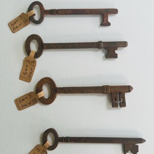 May include: A collection of six antique keys with varying designs and shapes. Each key is attached to a small tag with handwritten text. The keys are arranged vertically against a white background, showcasing their aged, rusty appearance.