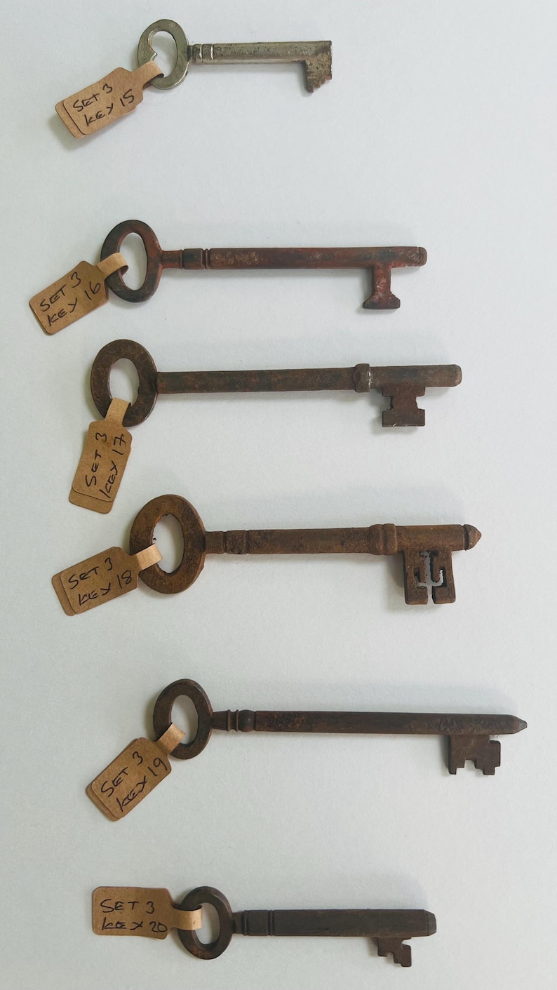 May include: A collection of six antique keys with varying designs and shapes. Each key is attached to a small tag with handwritten text. The keys are arranged vertically against a white background, showcasing their aged, rusty appearance.