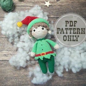 May include: A crocheted elf doll with a green outfit, red hat, and brown hair. The doll is lying on a white fluffy surface. The text "PDF PATTERN ONLY" is visible in the background.