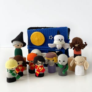 May include: A collection of handmade crochet dolls, each with unique features and outfits. The dolls are arranged in front of a blue and black crocheted book cover with a yellow sun and white star. The dolls are in various colors.