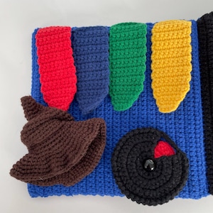 May include: A blue crocheted item with red, blue, green, and yellow shapes. A brown crocheted hat and a black circular shape with a red accent are also present. The item is likely a handmade craft or toy.