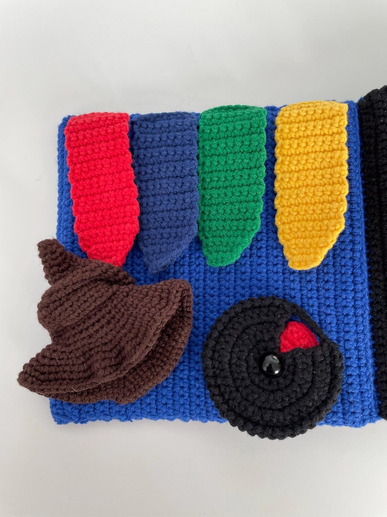 May include: A blue crocheted item with red, blue, green, and yellow shapes. A brown crocheted hat and a black circular shape with a red accent are also present. The item is likely a handmade craft or toy.
