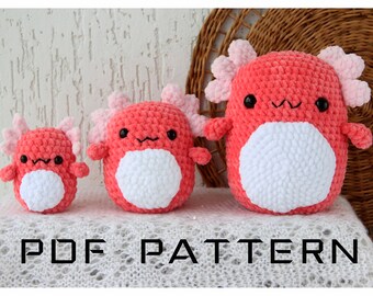 May include: Three crocheted axolotl plushies in different sizes. The plushies are pink and white with black eyes. The plushies are sitting on a white surface with the text "PDF PATTERN" below them.