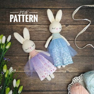 May include: PDF pattern for crocheting two bunny amigurumi dolls. One doll is wearing a light blue tulle skirt with white floral print and the other is wearing a purple tulle skirt with pink and white floral print.
