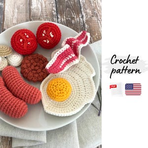 Puede incluir: Un plato de desayuno tejido a ganchillo, que incluye dos mitades de tomate rojo, tocino, un huevo frito, salchichas y una hamburguesa. El texto "Crochet pattern" es visible.