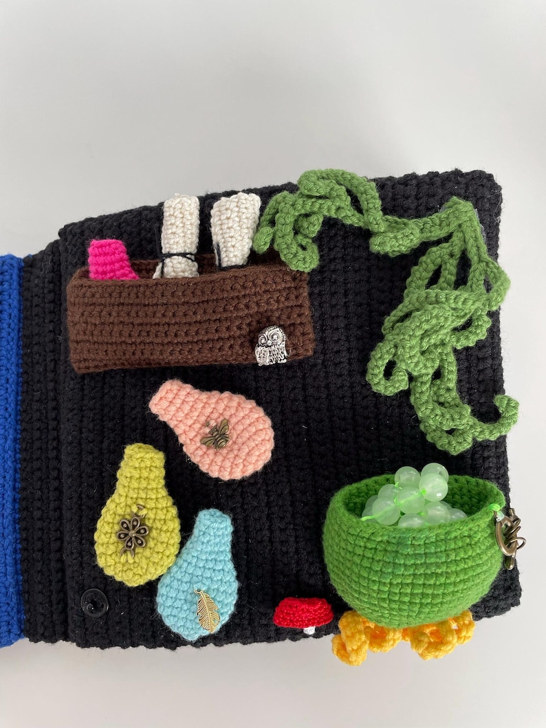May include: A black crocheted textile with various colorful crocheted appliques. Features include a brown basket with pink and white items, green vines, pear shapes, a green bowl with beads, and a red mushroom.