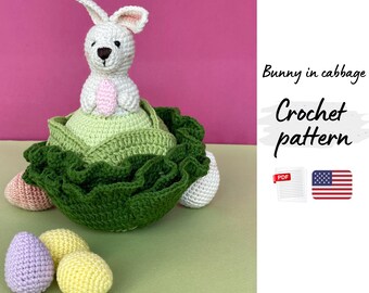 May include: A crocheted Easter bunny with a pink belly sits atop a green cabbage. The bunny is white with pink inner ears. Surrounding the cabbage are crocheted Easter eggs in pastel colors. The image includes the text "Bunny in cabbage Crochet pattern".