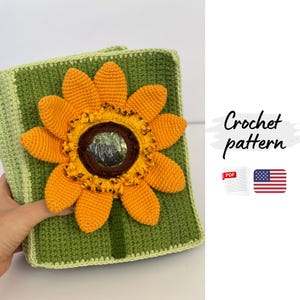 Puede incluir: Un cuadrado verde tejido a ganchillo con una gran aplicación de girasol naranja y amarillo. El girasol tiene un centro marrón. El texto "Crochet pattern" es visible.