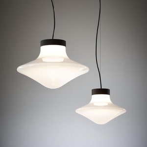 May include: Two white glass pendant lights with black cords and black metal bases. The lights are shaped like a saucer or a shallow bowl.