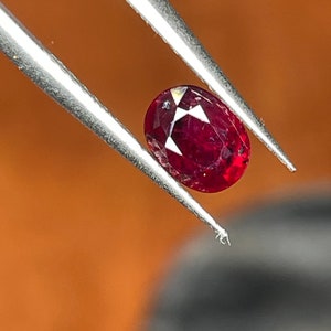Può includere: Una pietra preziosa ovale di colore rosso scuro tenuta da una pinzetta. La pietra preziosa è sfaccettata e ha un'alta lucentezza.