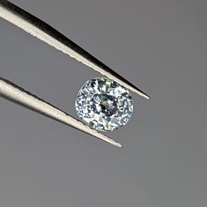 Peut inclure: Une pierre précieuse ronde de couleur bleu clair tenue par des pinces. La pierre précieuse a une taille facetée et une apparence claire et transparente.