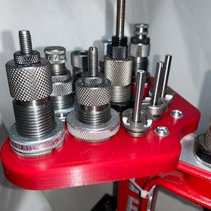 May include: A red reloading press with a variety of reloading dies. The dies are made of metal and have a knurled finish. The press is made of metal and has a black finish.