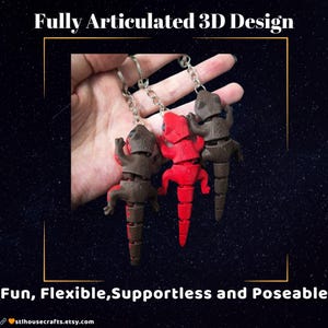 以下が含まれることがあります： 3Dプリントされた、関節が動くトカゲのキーホルダーが3つ。1つは赤、2つは茶色です。キーホルダーは銀色のチェーンから吊り下げられています。画像には「Fully Articulated 3D Design」と「Fun, Flexible, Supportless and Poseable」という文字が含まれています。
