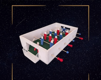 Op de afbeelding: Een 3D-printbare tafelvoetbaltafel met rode en blauwe spelerfiguren. De witte tafel heeft een groen speelveld en een klein net. De afbeelding bevat de tekst "3D PRINTABLE SUCCER GAME".