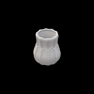 Pode incluir: Um pequeno vaso branco com uma apar&ecirc;ncia texturizada e tricotada. O vaso tem uma base arredondada e uma abertura ligeiramente alargada. A superf&iacute;cie apresenta um padr&atilde;o de chevr&atilde;o repetido, adicionando interesse visual ao design. O fundo &eacute; preto s&oacute;lido.