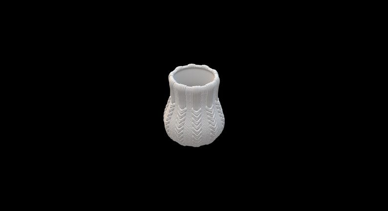 Pode incluir: Um pequeno vaso branco com uma apar&ecirc;ncia texturizada e tricotada. O vaso tem uma base arredondada e uma abertura ligeiramente alargada. A superf&iacute;cie apresenta um padr&atilde;o de chevr&atilde;o repetido, adicionando interesse visual ao design. O fundo &eacute; preto s&oacute;lido.
