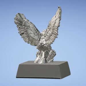 May include: A silver eagle statue with its wings spread wide, perched on a silver base. The eagle is facing away from the viewer, with its head turned to the side.
