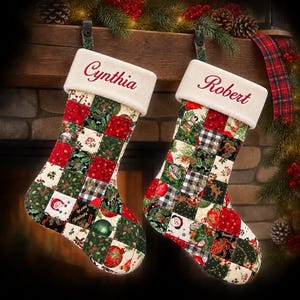 May include: Two Christmas stockings featuring a patchwork design of red, green, and white fabric squares with holiday patterns including snowmen, ornaments, and holly. Each stocking has a white plush cuff embroidered with the names Cynthia and Robert.