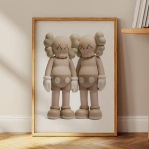 May include: Framed artwork showing two beige cartoon figures with X-shaped eyes. The figures are side by side, wearing white gloves and shorts. The artwork is in a wooden frame, leaning against a wall. The frame is approximately 60 cm in height.