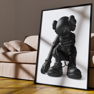 Puede incluir: Ilustraci&oacute;n en blanco y negro de un personaje de dibujos animados con una cabeza grande y un cuerpo peque&ntilde;o, sentado con las piernas cruzadas y las manos sobre las rodillas. El personaje lleva una camisa y pantalones negros, y tiene una X negra en la frente.