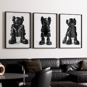 Puede incluir: Tres impresiones enmarcadas en blanco y negro de un personaje de dibujos animados con diferentes poses. El personaje lleva un atuendo negro y tiene una cara en blanco y negro. Las impresiones est&aacute;n colgadas en una pared blanca.