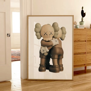May include: A framed print of two brown and beige cartoon figures hugging each other. The figures have large heads with X-shaped eyes and small mouths. The print is on a white background.