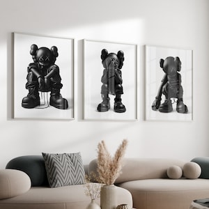 Puede incluir: Tres impresiones enmarcadas en blanco y negro de un personaje de dibujos animados con diferentes poses. El personaje lleva un atuendo negro y tiene una X negra por ojos. Las impresiones est&aacute;n colgadas en una pared blanca sobre un sof&aacute; gris claro.