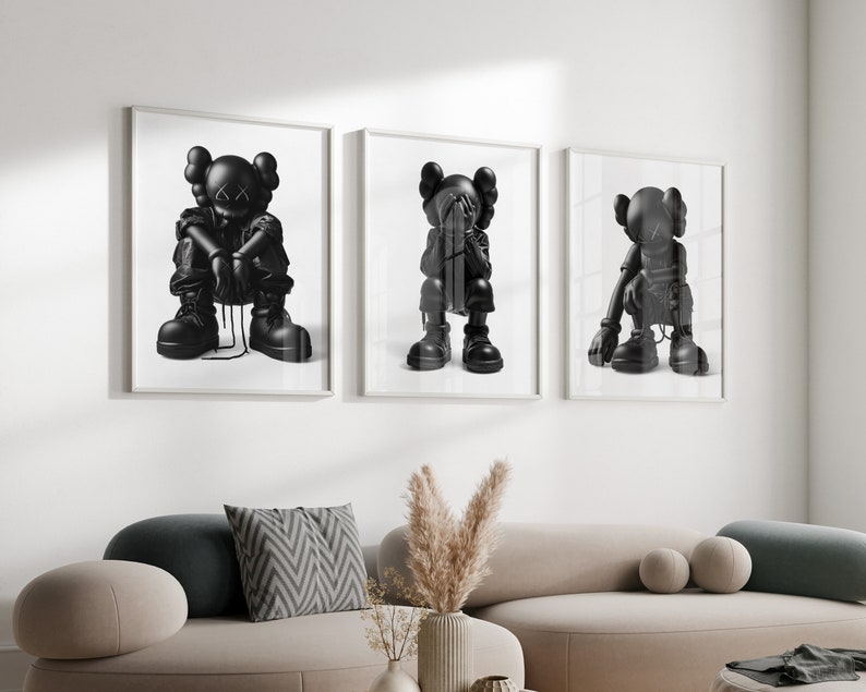 Puede incluir: Tres impresiones enmarcadas en blanco y negro de un personaje de dibujos animados con diferentes poses. El personaje lleva un atuendo negro y tiene una X negra por ojos. Las impresiones est&aacute;n colgadas en una pared blanca sobre un sof&aacute; gris claro.