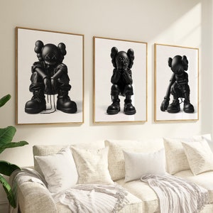Puede incluir: Tres impresiones enmarcadas en blanco y negro de figuras de dibujos animados con las manos cubri&eacute;ndose la cara. Las figuras est&aacute;n en diferentes poses, y las impresiones est&aacute;n colgadas en una pared blanca sobre un sof&aacute; blanco.