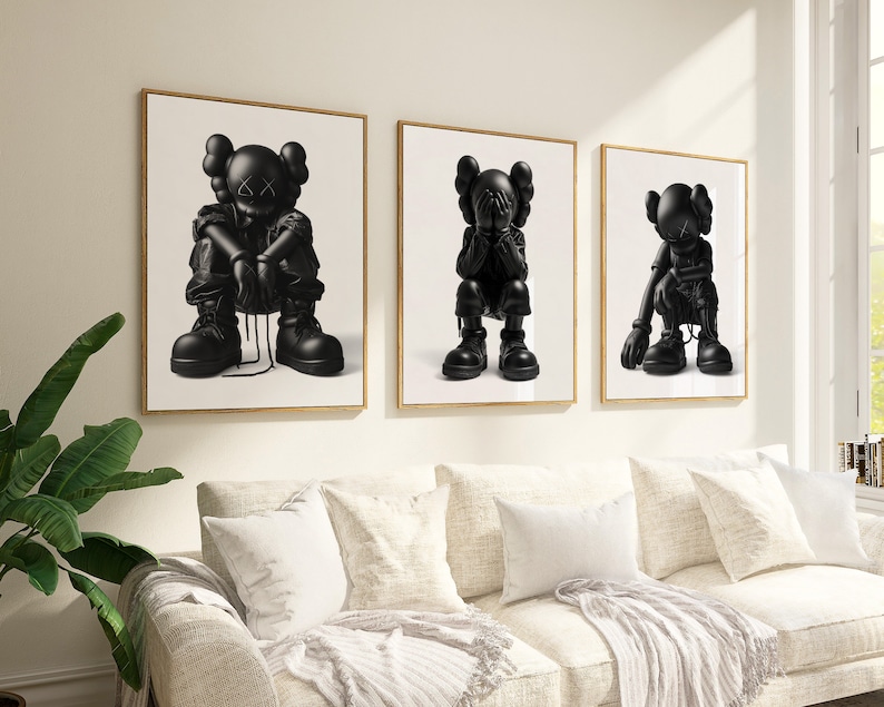 Puede incluir: Tres impresiones enmarcadas en blanco y negro de figuras de dibujos animados con las manos cubri&eacute;ndose la cara. Las figuras est&aacute;n en diferentes poses, y las impresiones est&aacute;n colgadas en una pared blanca sobre un sof&aacute; blanco.