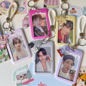 Può includere: Una collezione di porta badge in vari colori, ognuno con la foto di una persona. I porta badge sono decorati con ciondoli e attaccati a cordini bianchi intrecciati con portachiavi. Sono presenti anche adesivi e biglietti.