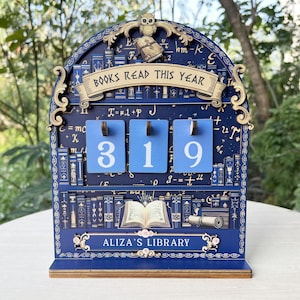 May include: A blue wooden bookshelf-themed counter displaying "BOOKS READ THIS YEAR" and the number "319". The counter has the text "ALIZA'S LIBRARY" at the bottom. An owl and a small book are at the top of the counter.
