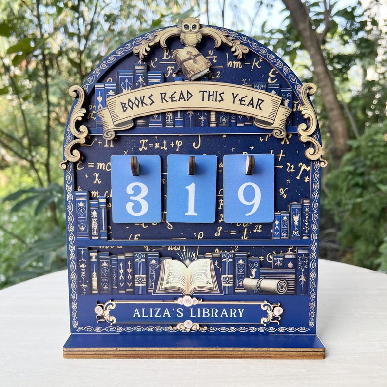 May include: A blue wooden bookshelf-themed counter displaying "BOOKS READ THIS YEAR" and the number "319". The counter has the text "ALIZA'S LIBRARY" at the bottom. An owl and a small book are at the top of the counter.