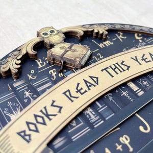 May include: A decorative wooden piece with the text "BOOKS READ THIS YEAR". The design includes an owl, a book, and a background with mathematical symbols and book illustrations. The color scheme is dark blue and gold.