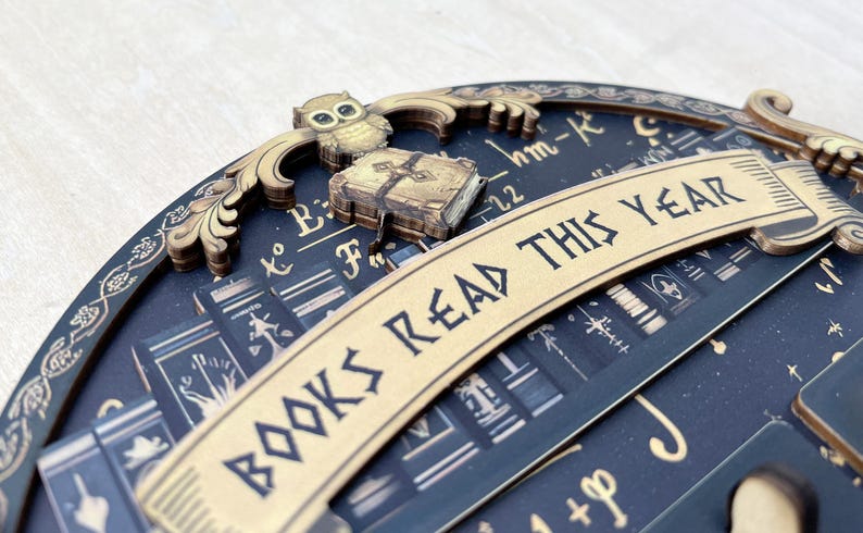 May include: A decorative wooden piece with the text "BOOKS READ THIS YEAR". The design includes an owl, a book, and a background with mathematical symbols and book illustrations. The color scheme is dark blue and gold.