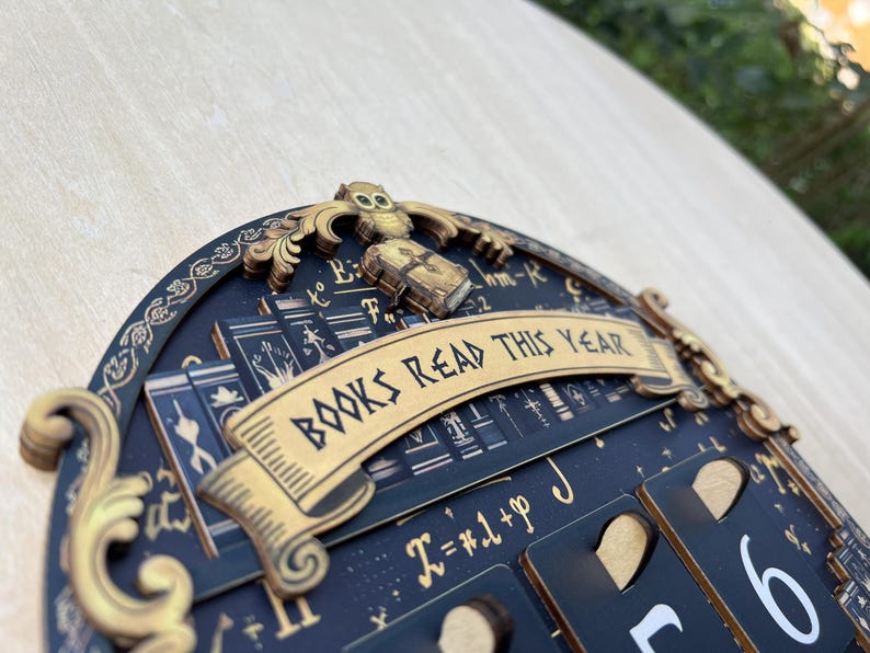 May include: A dark blue wooden wall decor with the text "BOOKS READ THIS YEAR" in gold. The decor features an owl, books, and a calendar-style design with numbers. The design has a vintage, antique aesthetic.