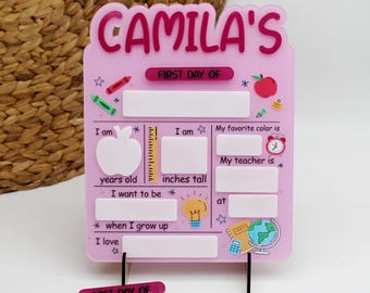 May include: Pink first day of school sign with the name "CAMILA'S" at the top. The sign has spaces for the child's age, height, favorite color, teacher's name, and what they want to be when they grow up. It also has a space for the child to write what they love.